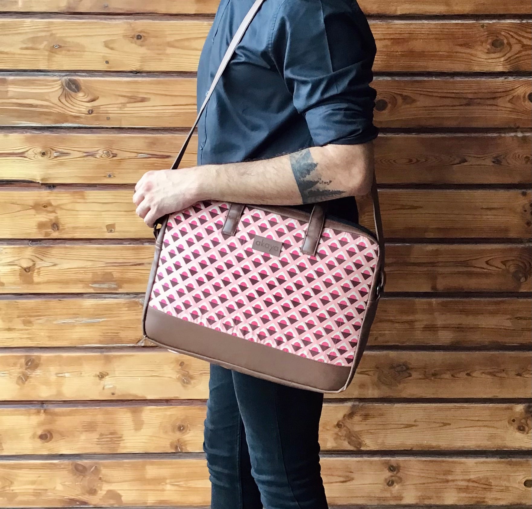 A man holding our Geoplay messenger bag with sling, against a backdrop of a wooden wall.