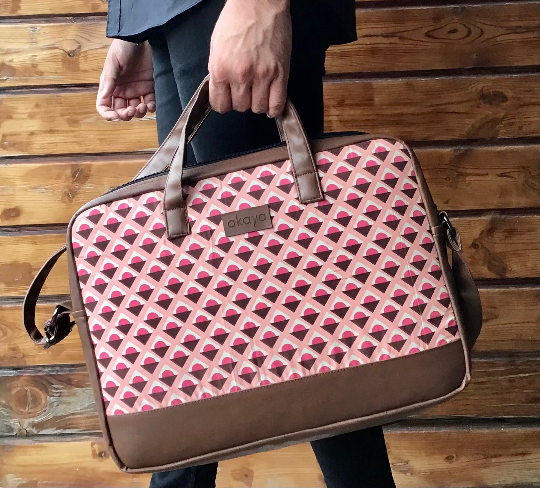 a man holding our Geoplay messenger bag with handle, against a backdrop of a wooden wall.