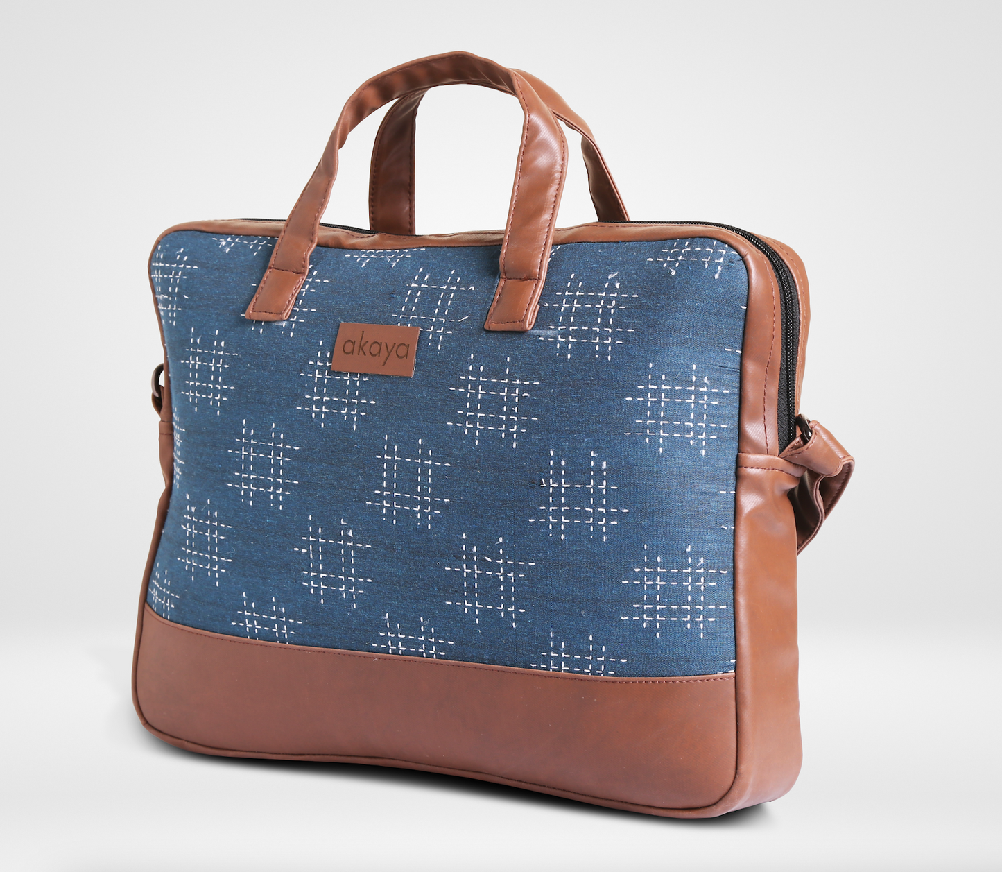 our laptop bag/ messenger bag with blue kantha design on and brown leather on handles, sides, bottom and sling on white background showing the side view, showing zip in the main pocket 